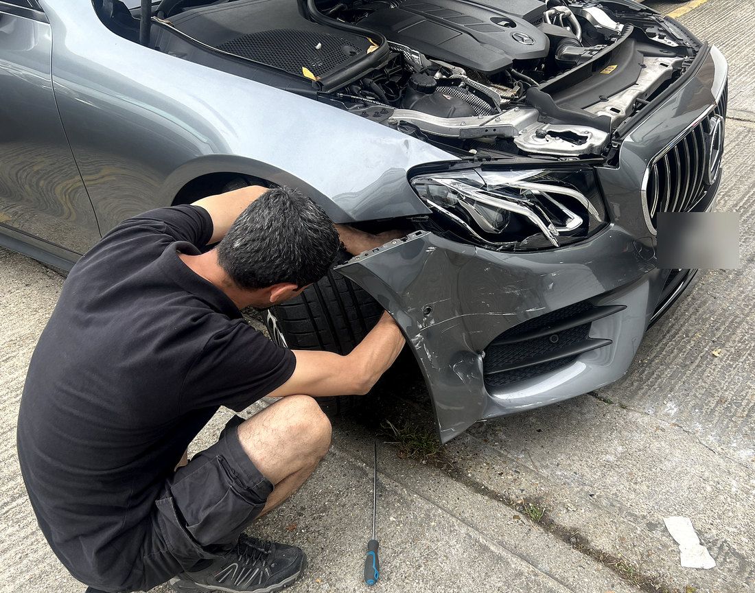 A technician examining the damaged front bumper of a grey Mercedes