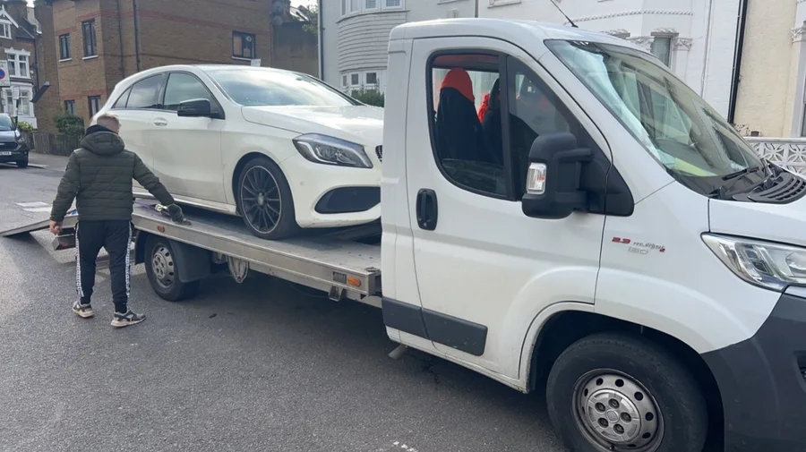 A white car being loaded onto a flatbed recovery truck on a residential street
